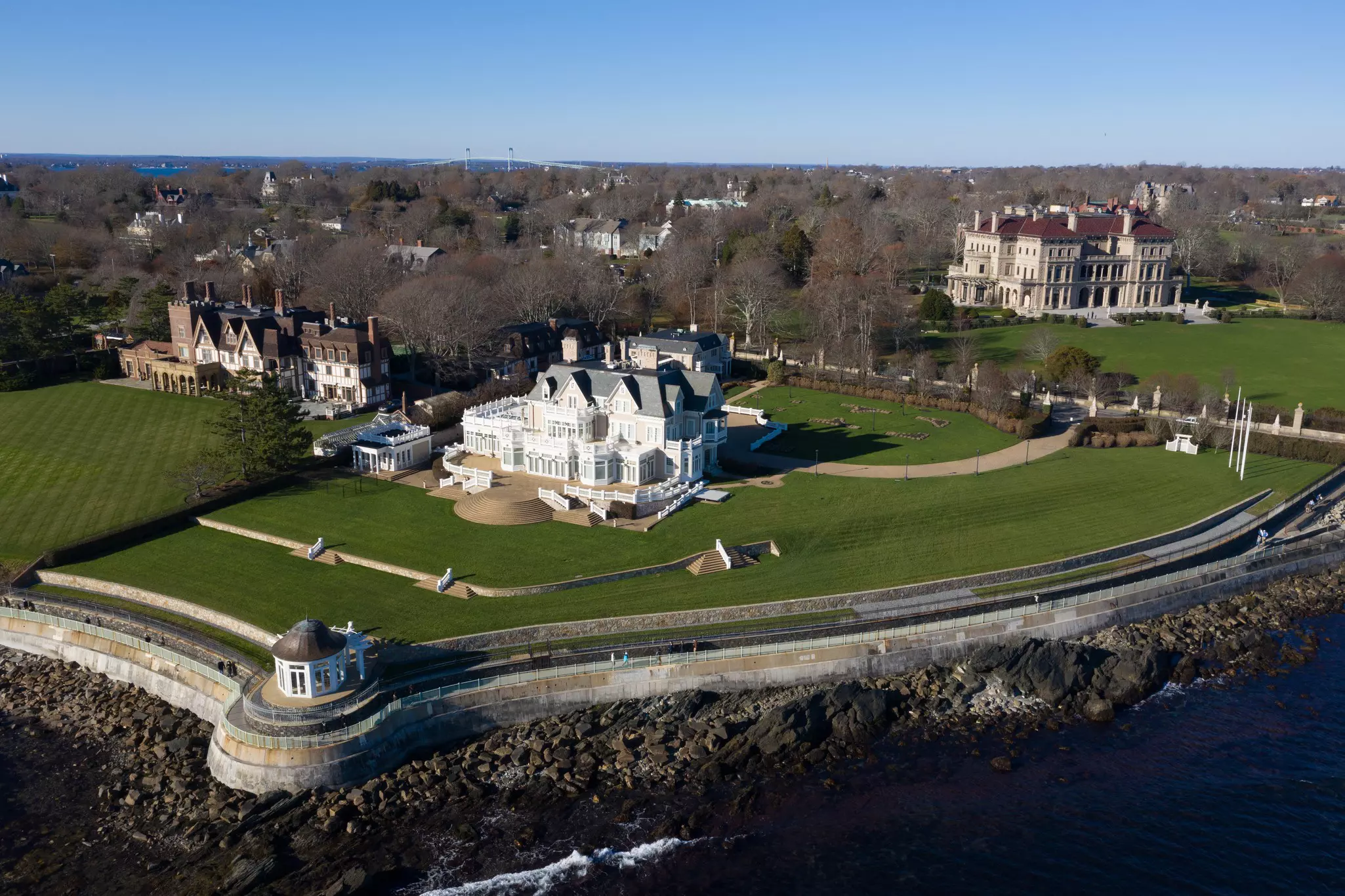 Aerial view of large mansion called The Breakers and its surrounding Cliff Walk, with other mansions in the distance.