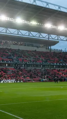 Green field with people in red filling stands in the background