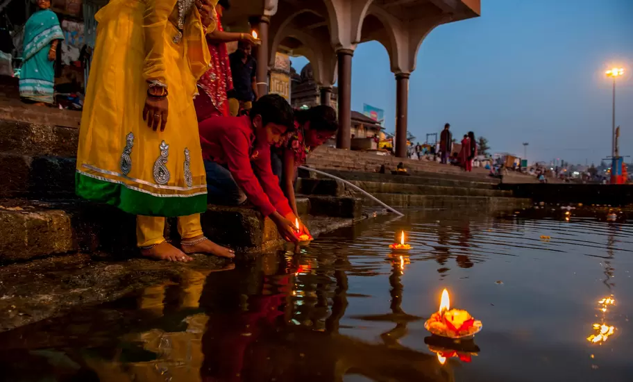 Pilgrims floating lit oil lamps with marigolds on the Godavari River from the ghat steps in Nashik, India, at dusk
