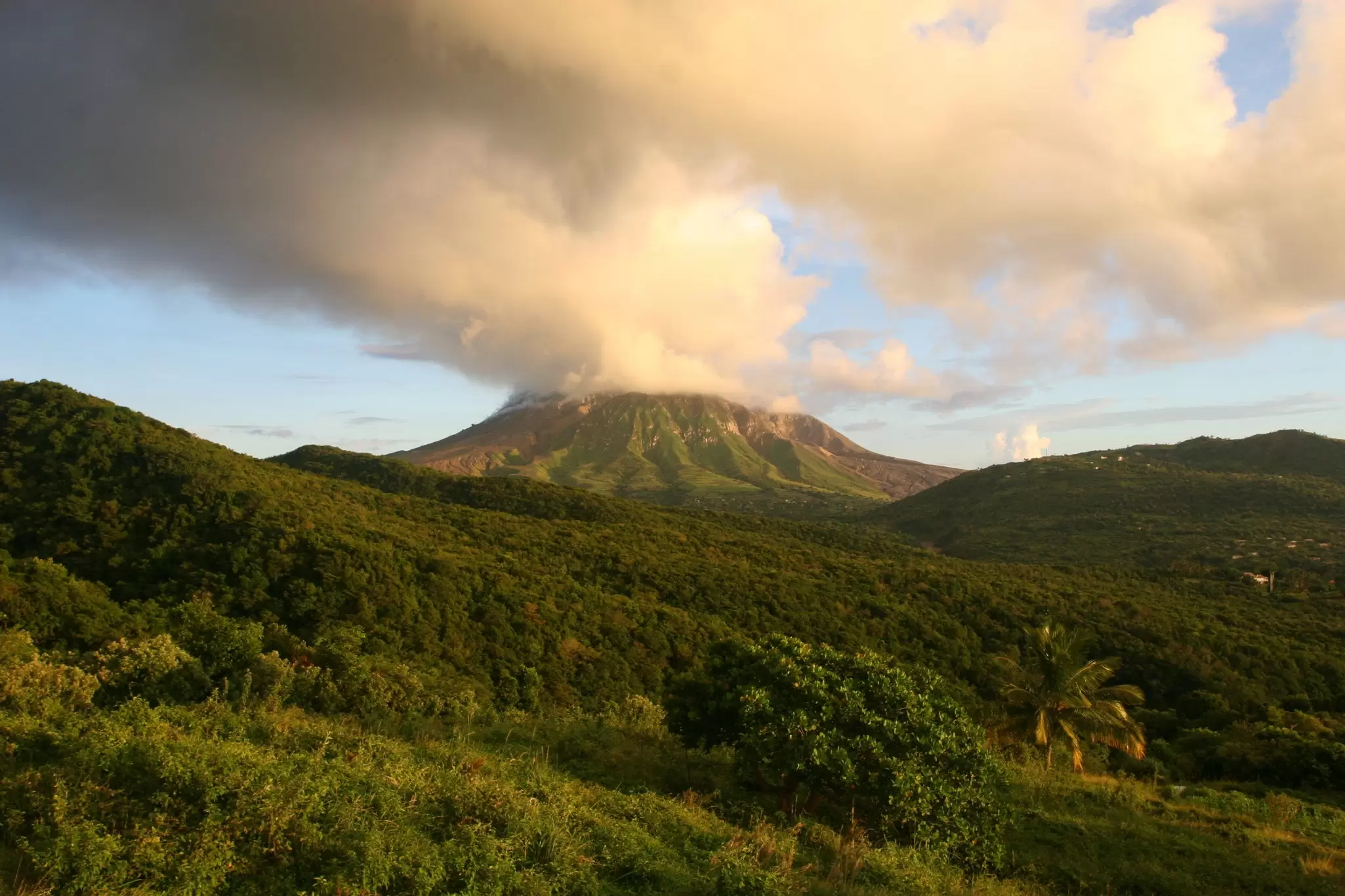 View up to Soufrière Hills Volcano with clouds above the cone and blue skies beyond