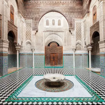 A courtyard in a building with detailed geometric tilework covering the floor, walls and surrounding a carved wooden doorway.