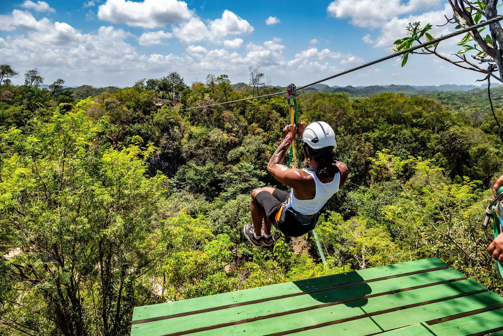 A person departs a green platform on a zipline over dense forest in a tropical location.