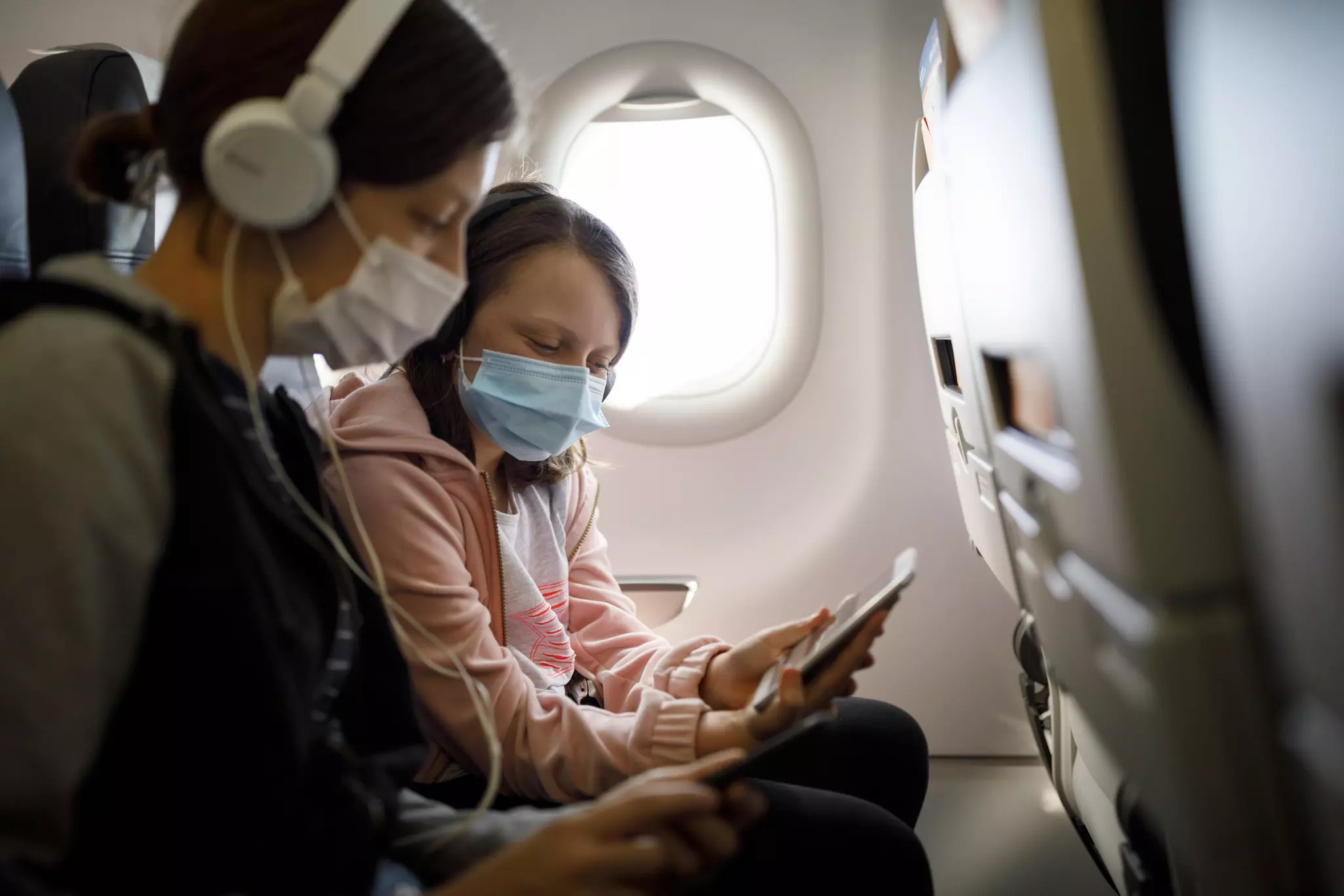 Kids with face protective mask using mobile phone in airplane.