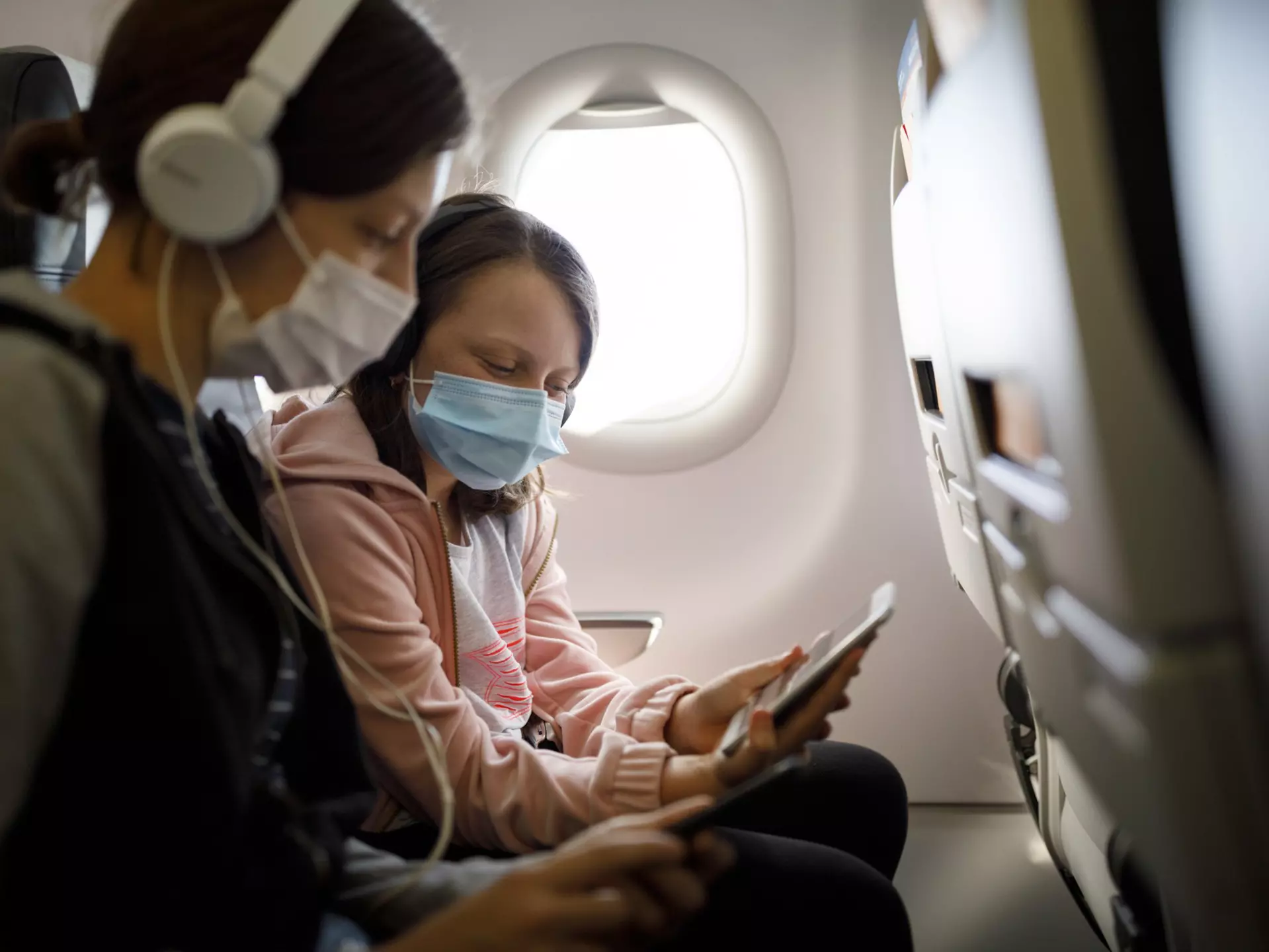 A mother and child wear face masks on an airplane
