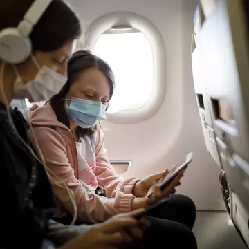 A mother and child wear face masks on an airplane