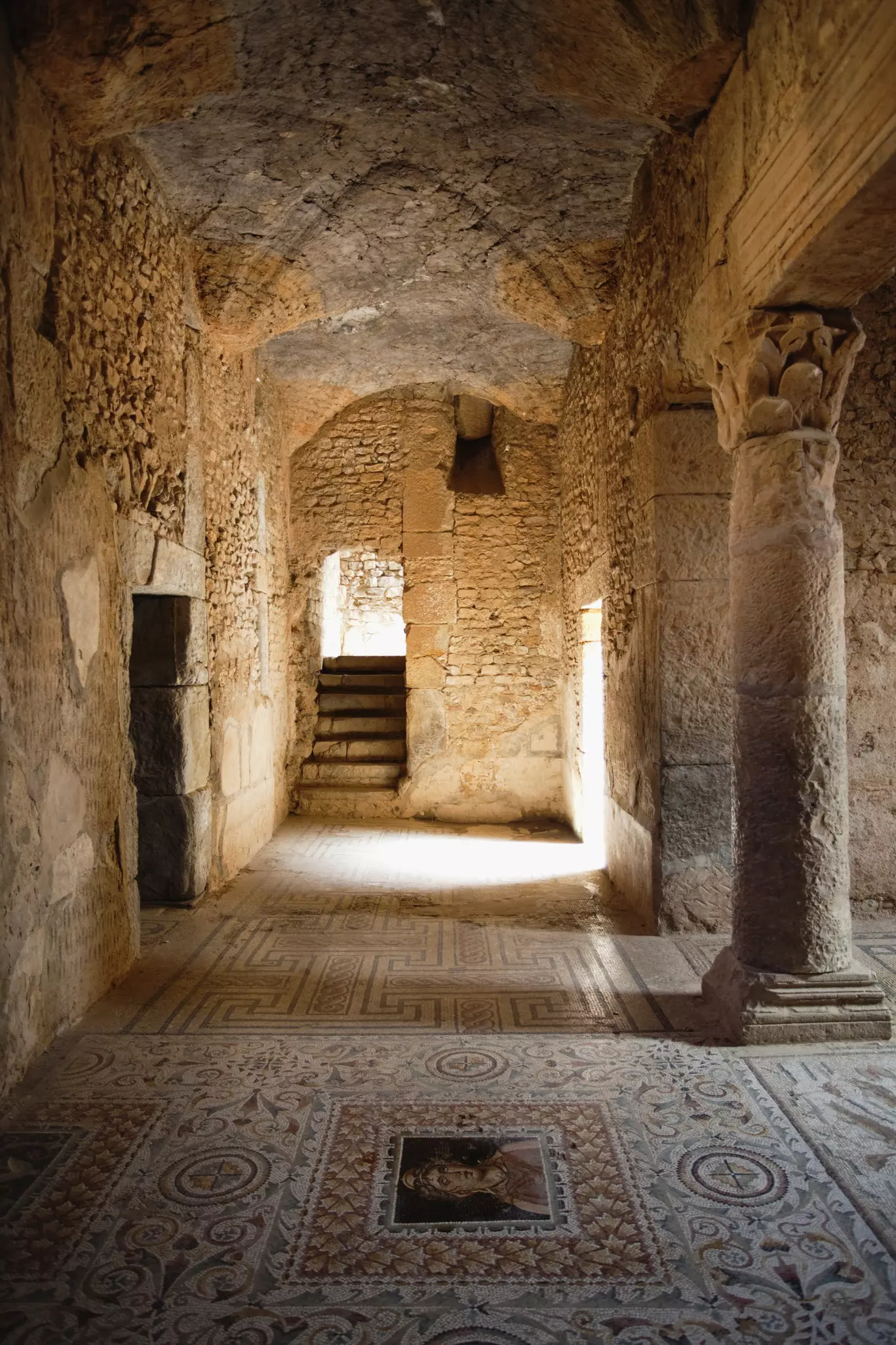 Ancient mosaics, including a picture of a woman, cover the floor of an ancient house.