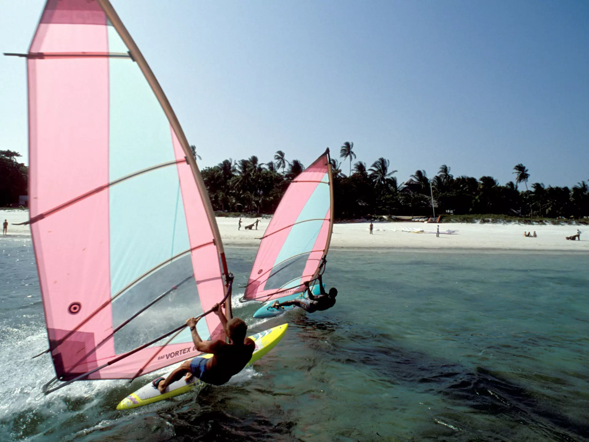 Two windsurfers just offshore from a lovely sandy beach.