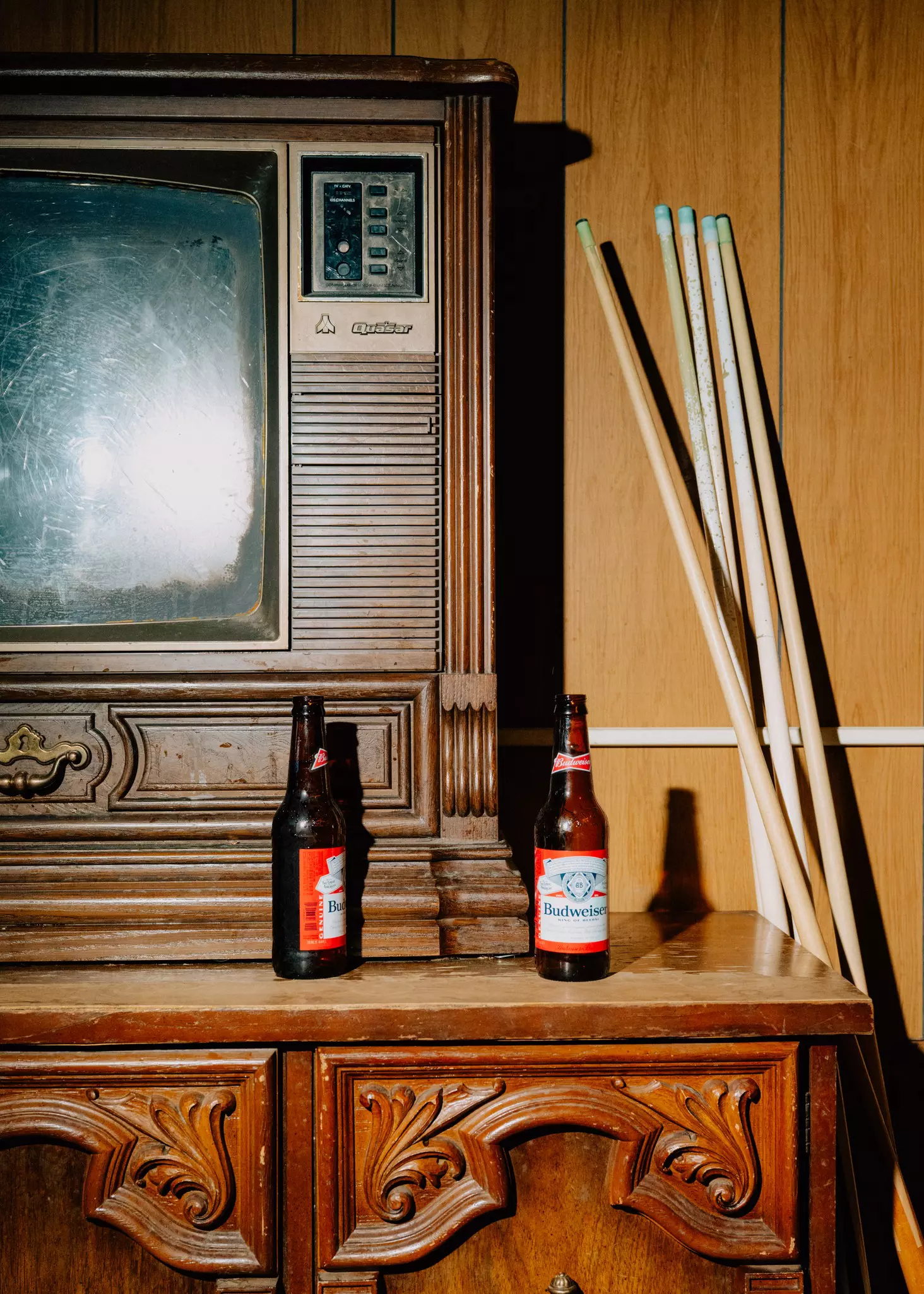 an old television sits on a wooden coffee table with two bottles of beer and a bunch of pool cues