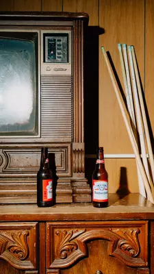 an old television sits on a wooden coffee table with two bottles of beer and a bunch of pool cues