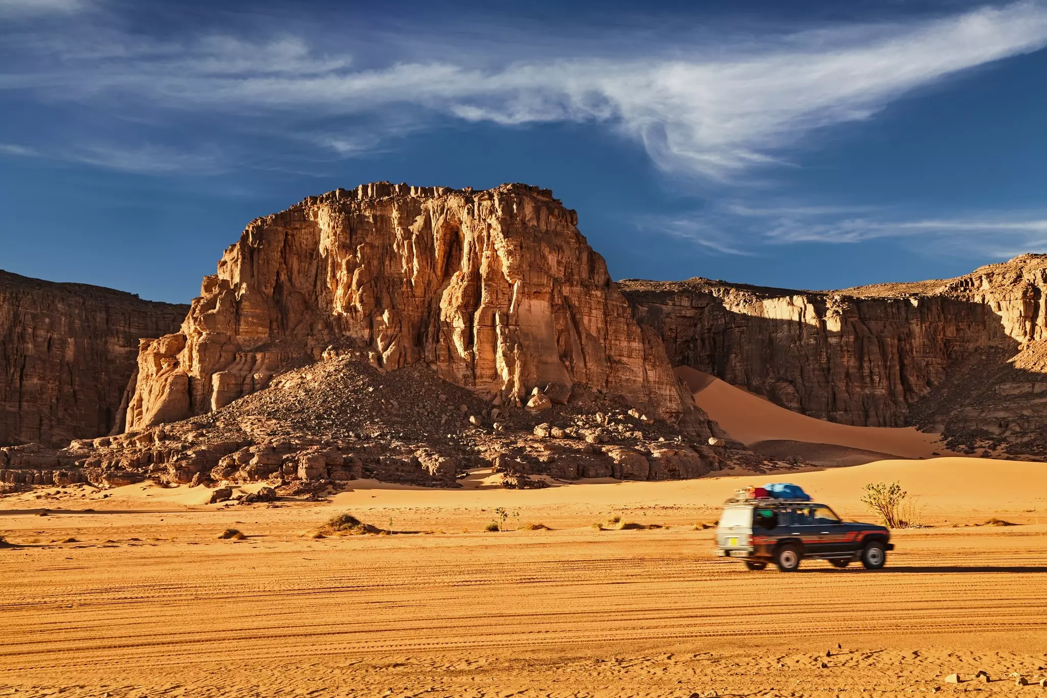 Road in Sahara Desert, a car drives among the rocks and sand dunes, Tadrart, Algeria.
