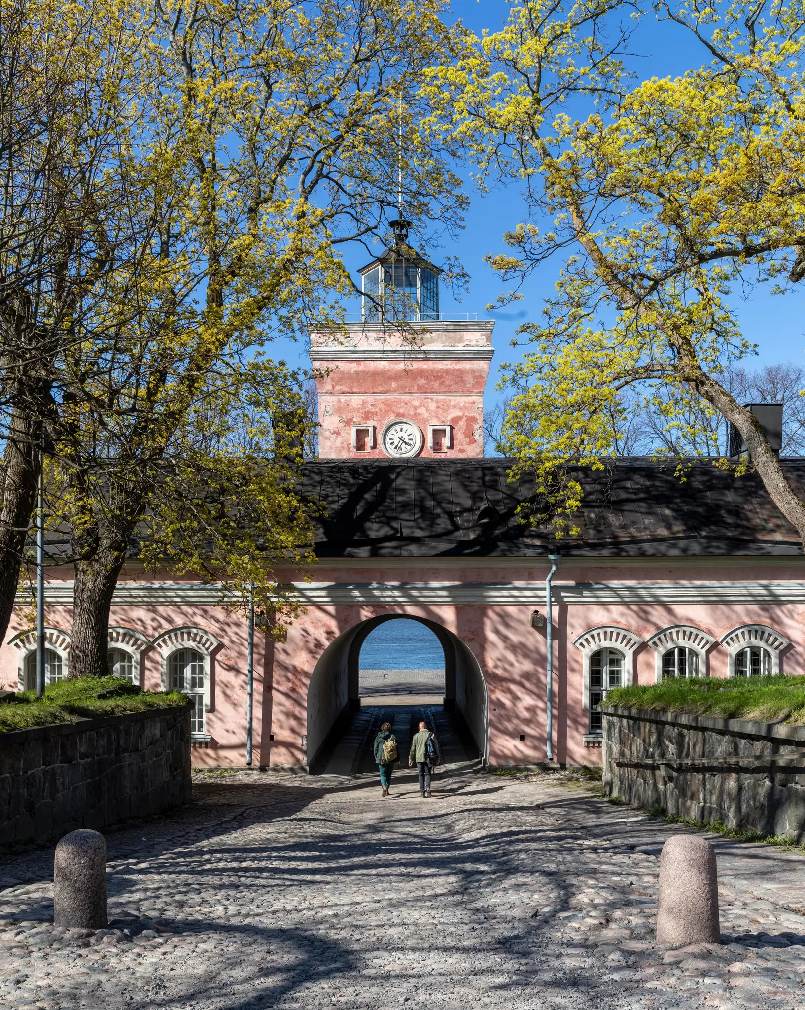 Helsinki, Finland - May 14, 2019: Two visitors on cobblestone drive heading toward entrance arch in jetty barracks,  Suomenlinna Island  License Type: media  Download Time: 2024-02-10T11:03:31.000Z  User: meg3348277  Is Editorial: Yes  purchase_order:   