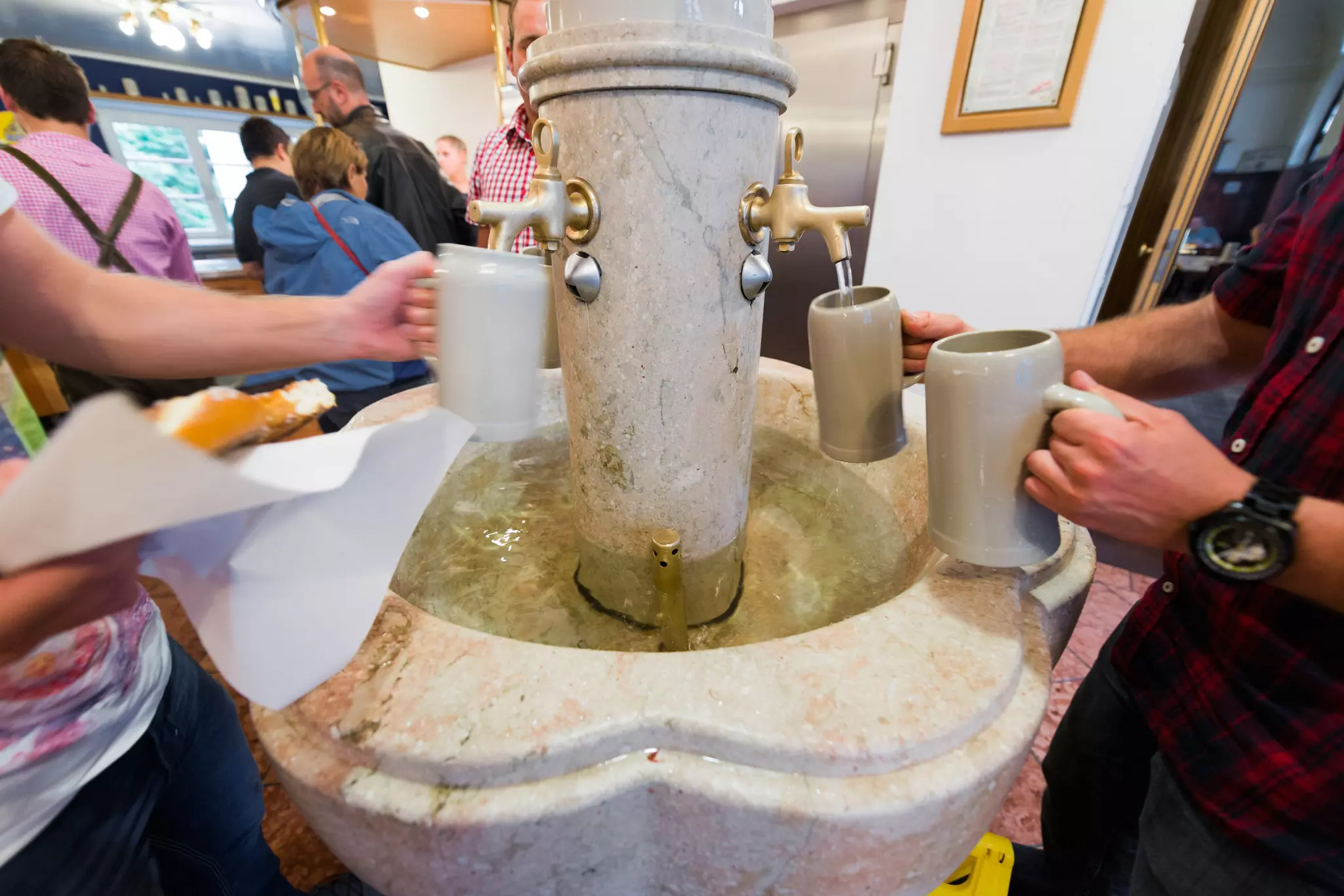 People filling ceramic steins from a marble fountain of beer with multiple spigots.
