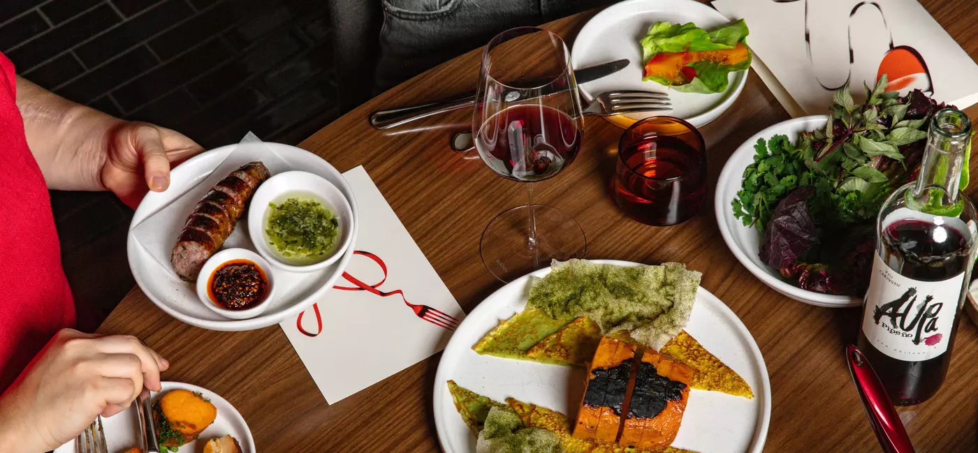 Plates of food spread out across a table with glasses of wine