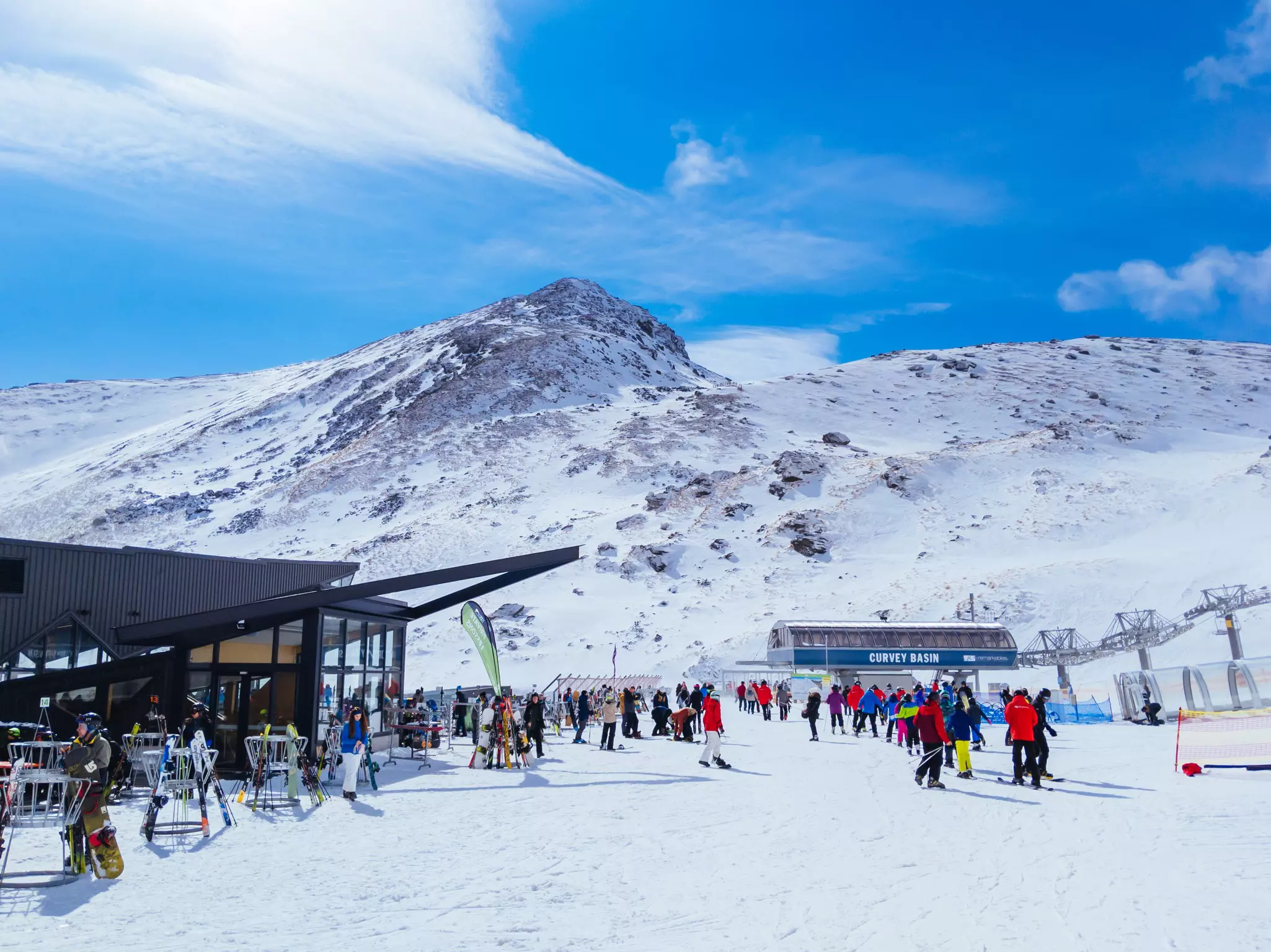 Skiers wait on the snow at the foot of a mountain for a ride up on a ski lift.