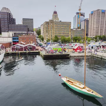 A sailboat leaves a harbor in a city with a busy waterfront