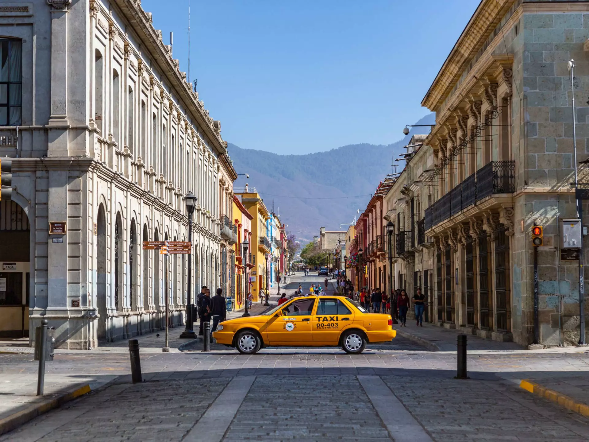 A yellow taxi drives across a cobbled street lined with historic buildings.