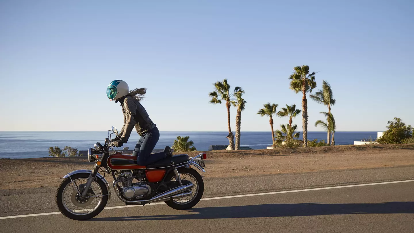 Young woman riding motorcycle on empty Malibu coastline road