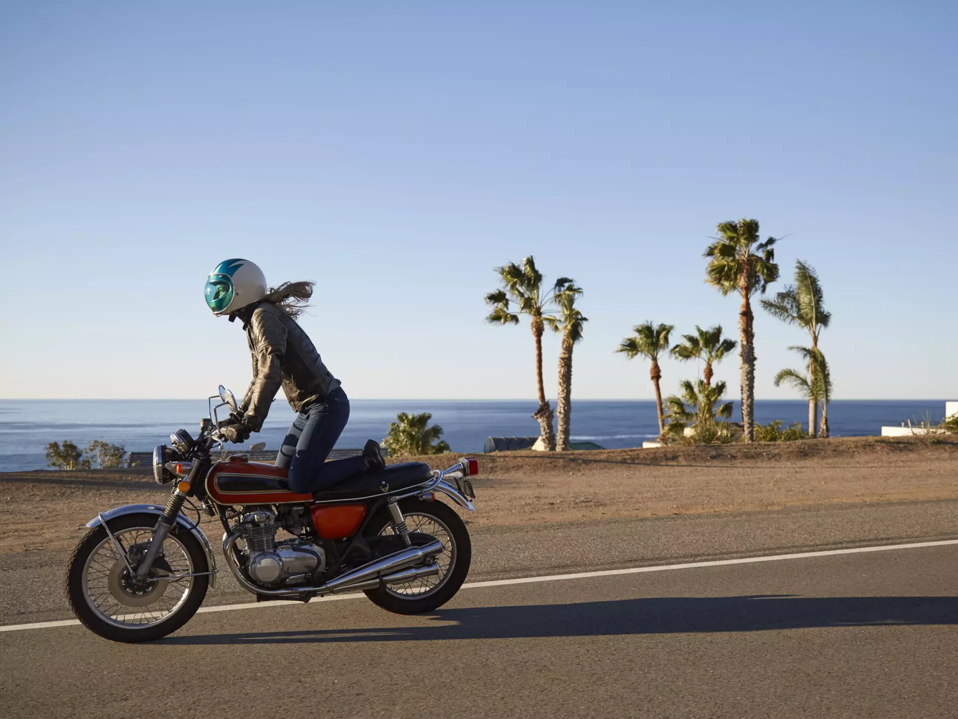 Young woman riding motorcycle on empty Malibu coastline road