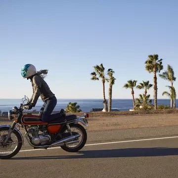Young woman riding motorcycle on empty Malibu coastline road