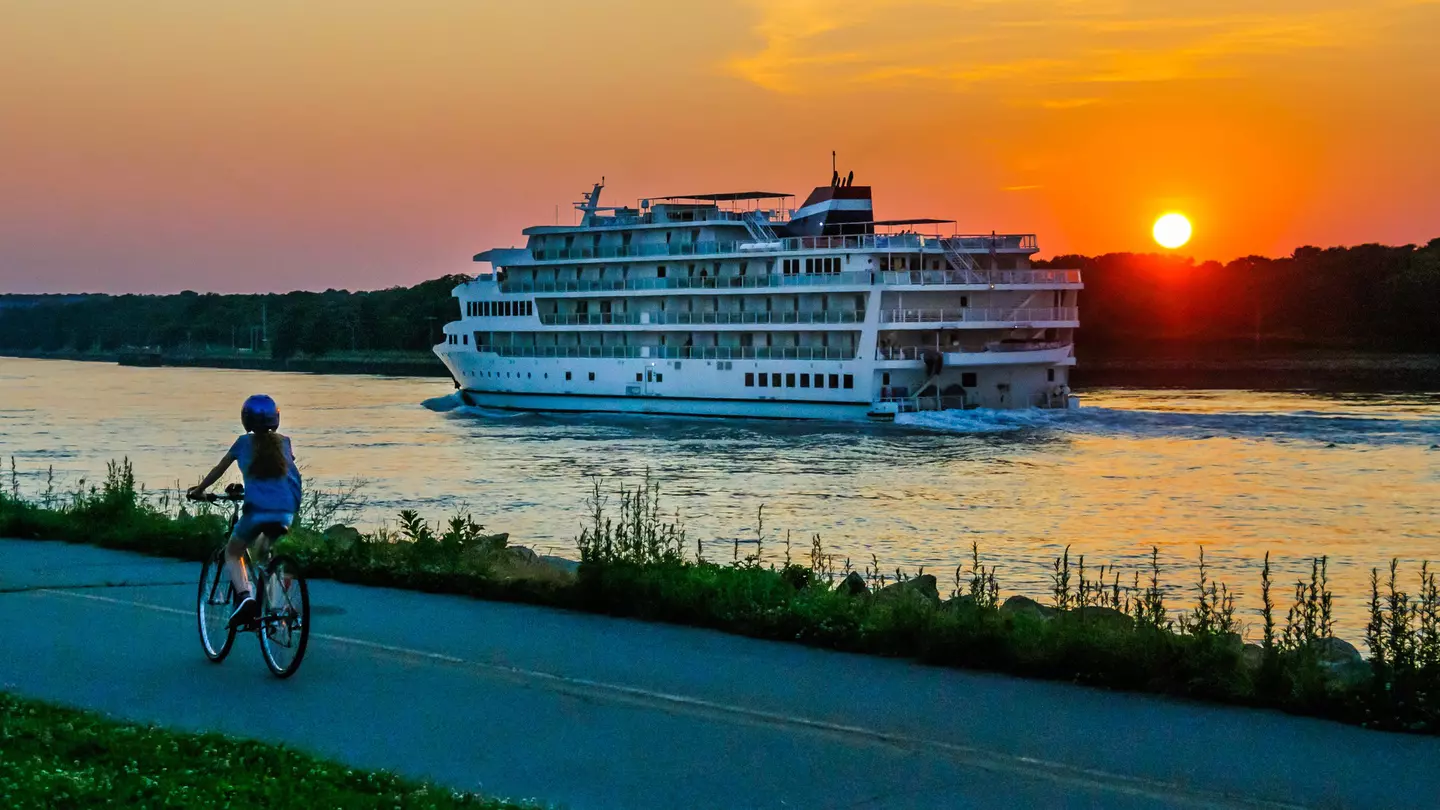 A young woman on a bicycle watches a cruise ship on the Cape Cod Canal