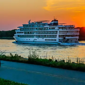 A young woman on a bicycle watches a cruise ship on the Cape Cod Canal