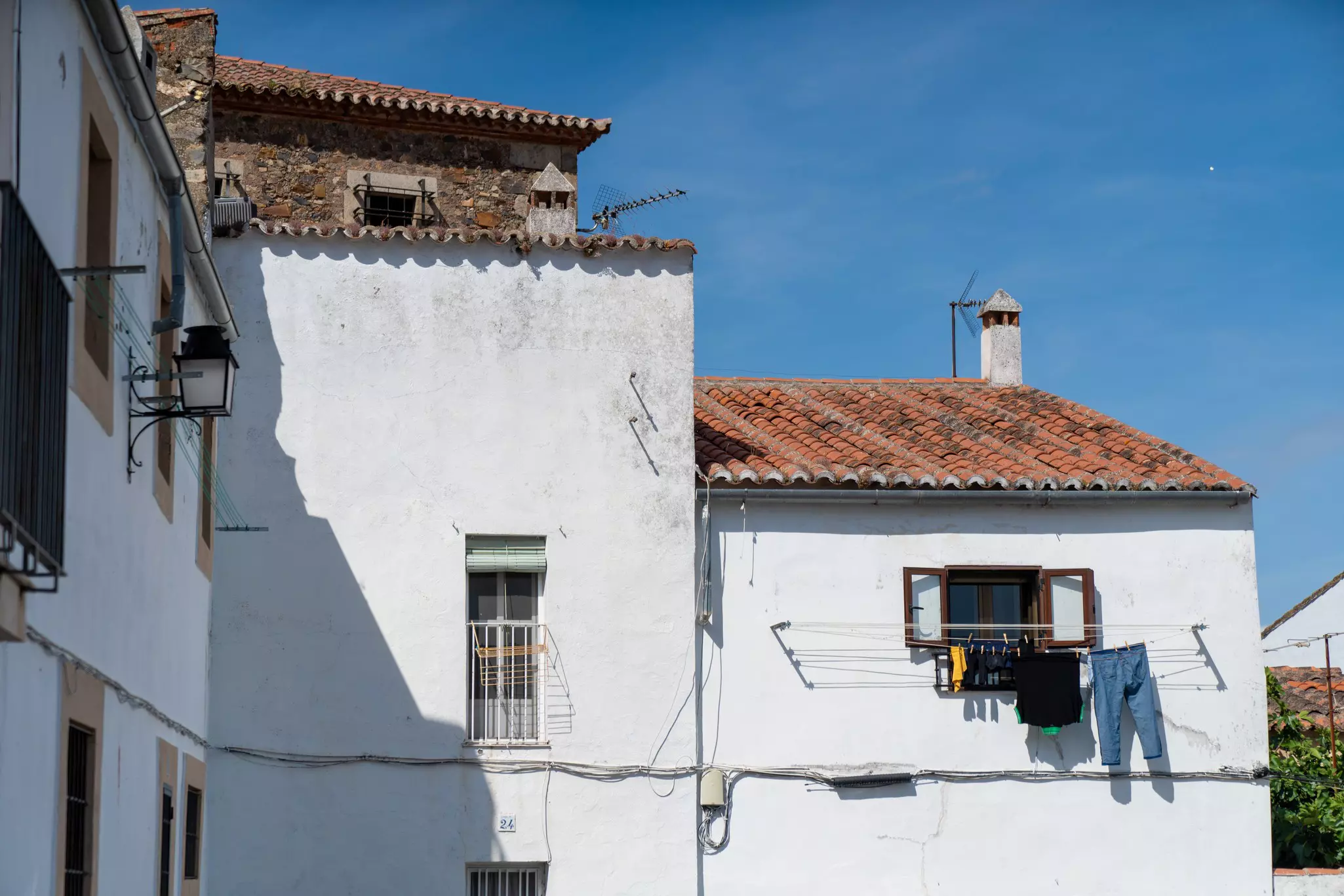 Laundry handing on a line out a window of a white stone house with terracotta roof on a sunny day.