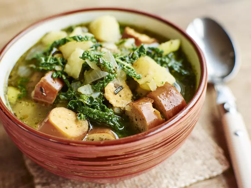 A terracotta bowl filled with sausage, kale and potato soup. 