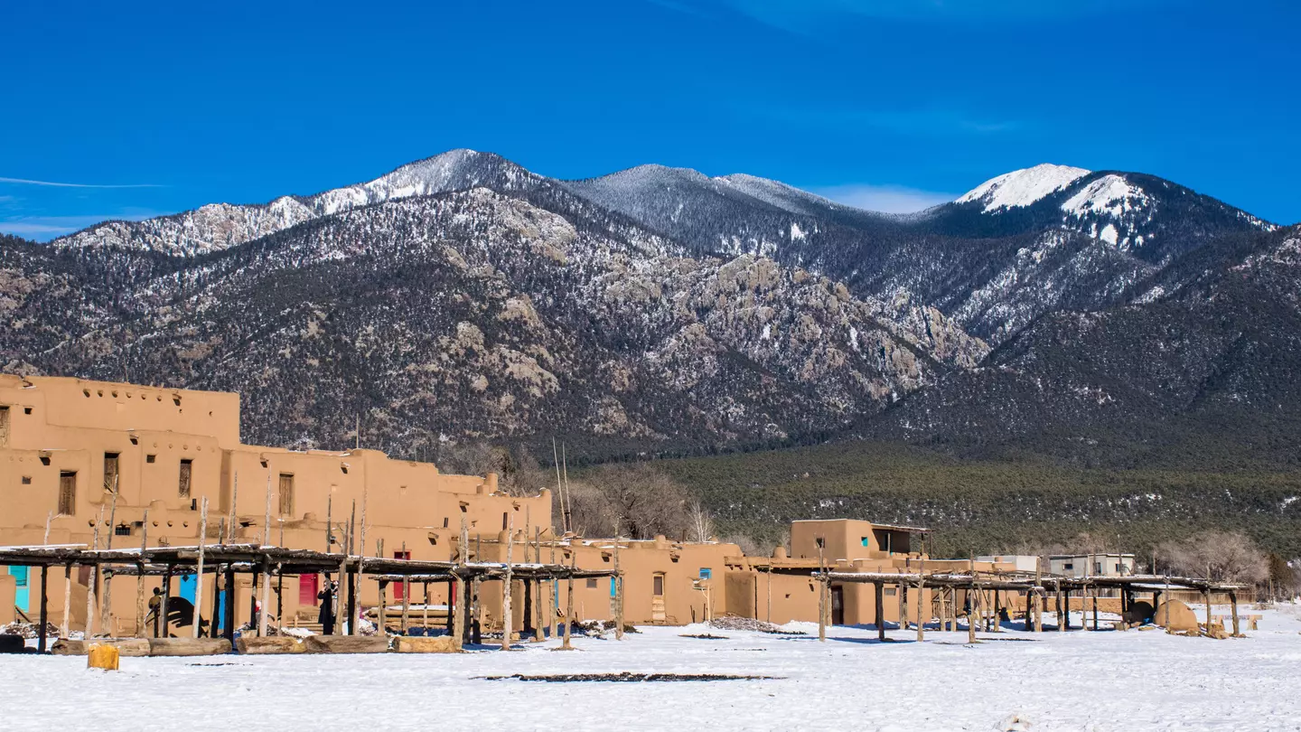 Low-rise red square buildings on a plateau at the foot of a snow-capped mountain range