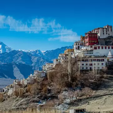 Buildings reach up to cover the top of a hillside; snowcapped mountains are in the background.