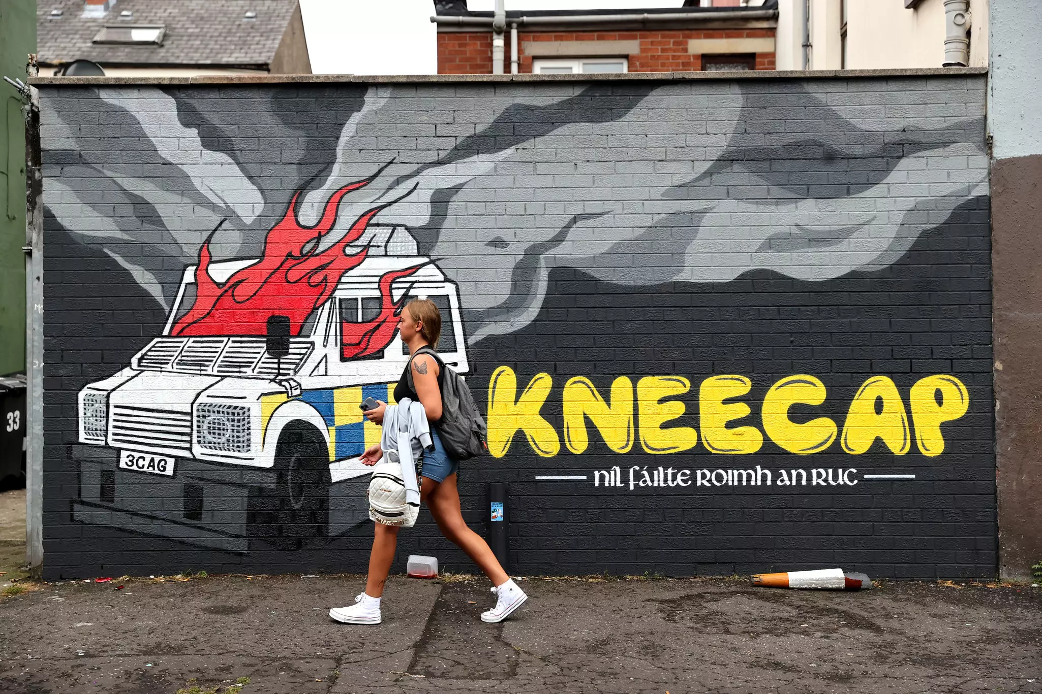 A person walks past a painted wall mural depicting a police car on fire.