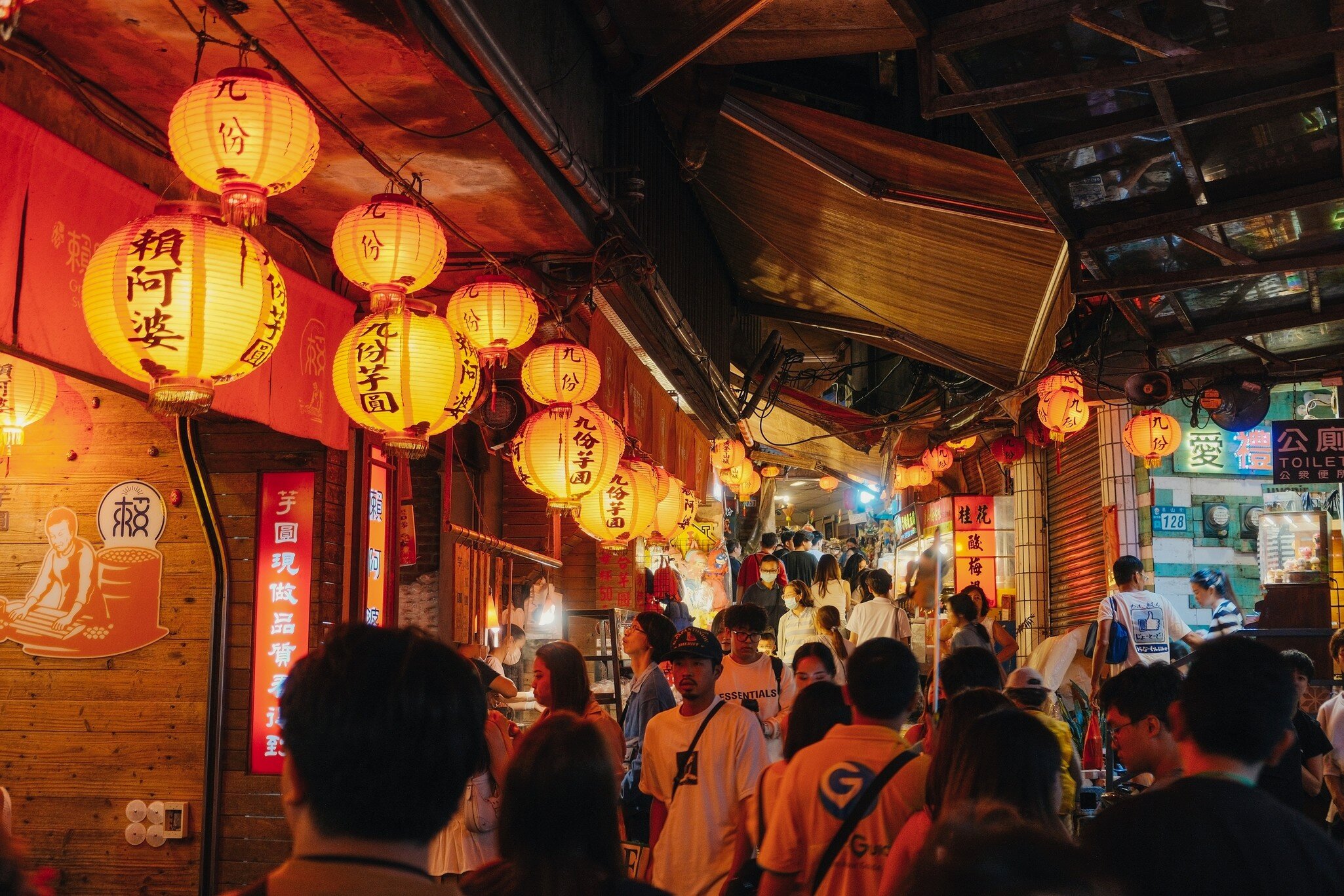Crowded Jishan street lined with stalls and vendors, lit up with glowing orange lanterns at night in Jiufen, Taiwan.