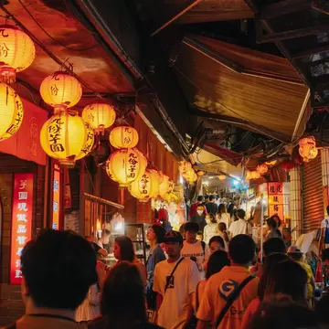 Crowded Jishan street lined with stalls and vendors, lit up with glowing orange lanterns at night in Jiufen, Taiwan.