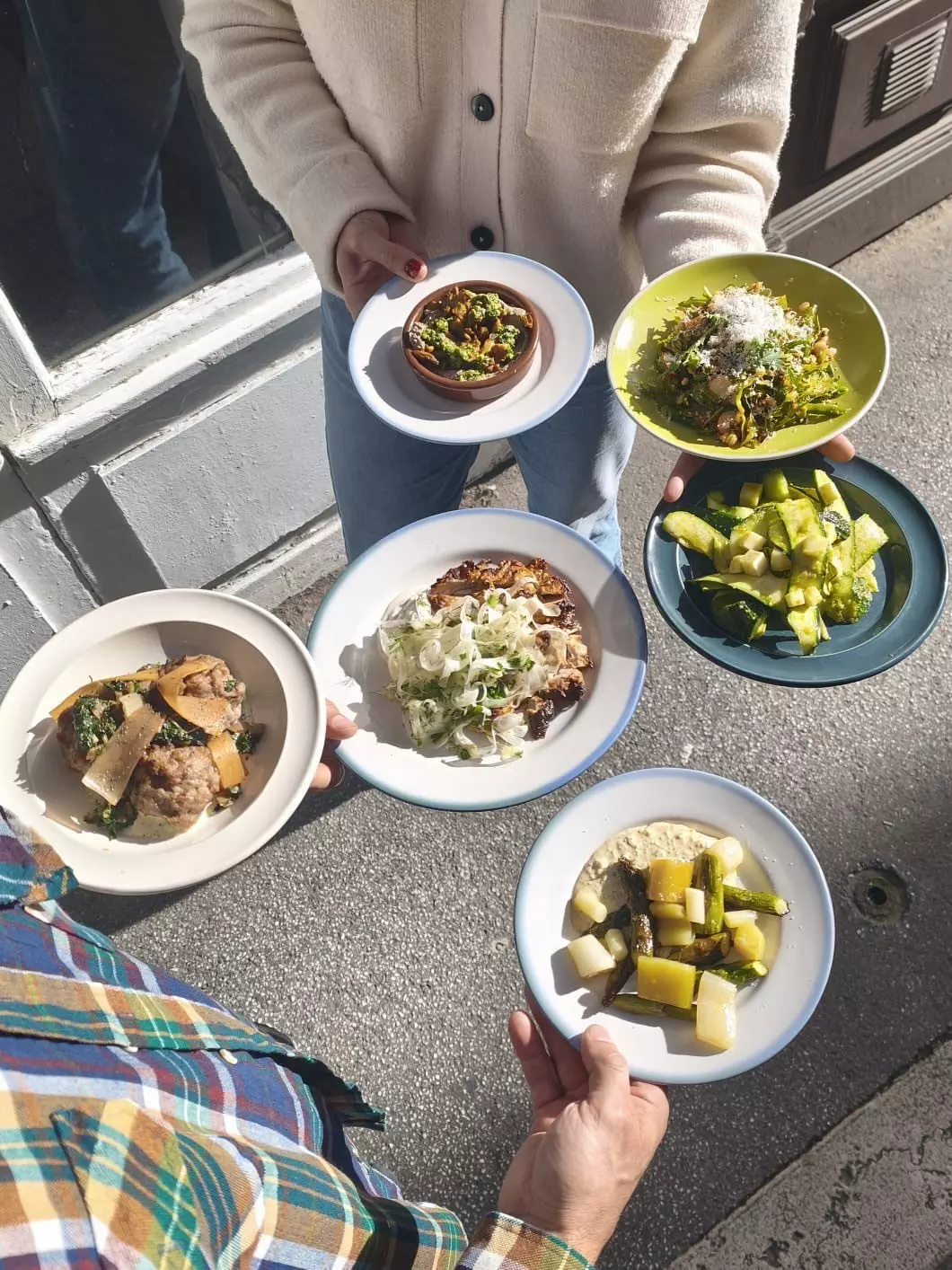 Two people hold out six beautifully presented dishes loaded with food.