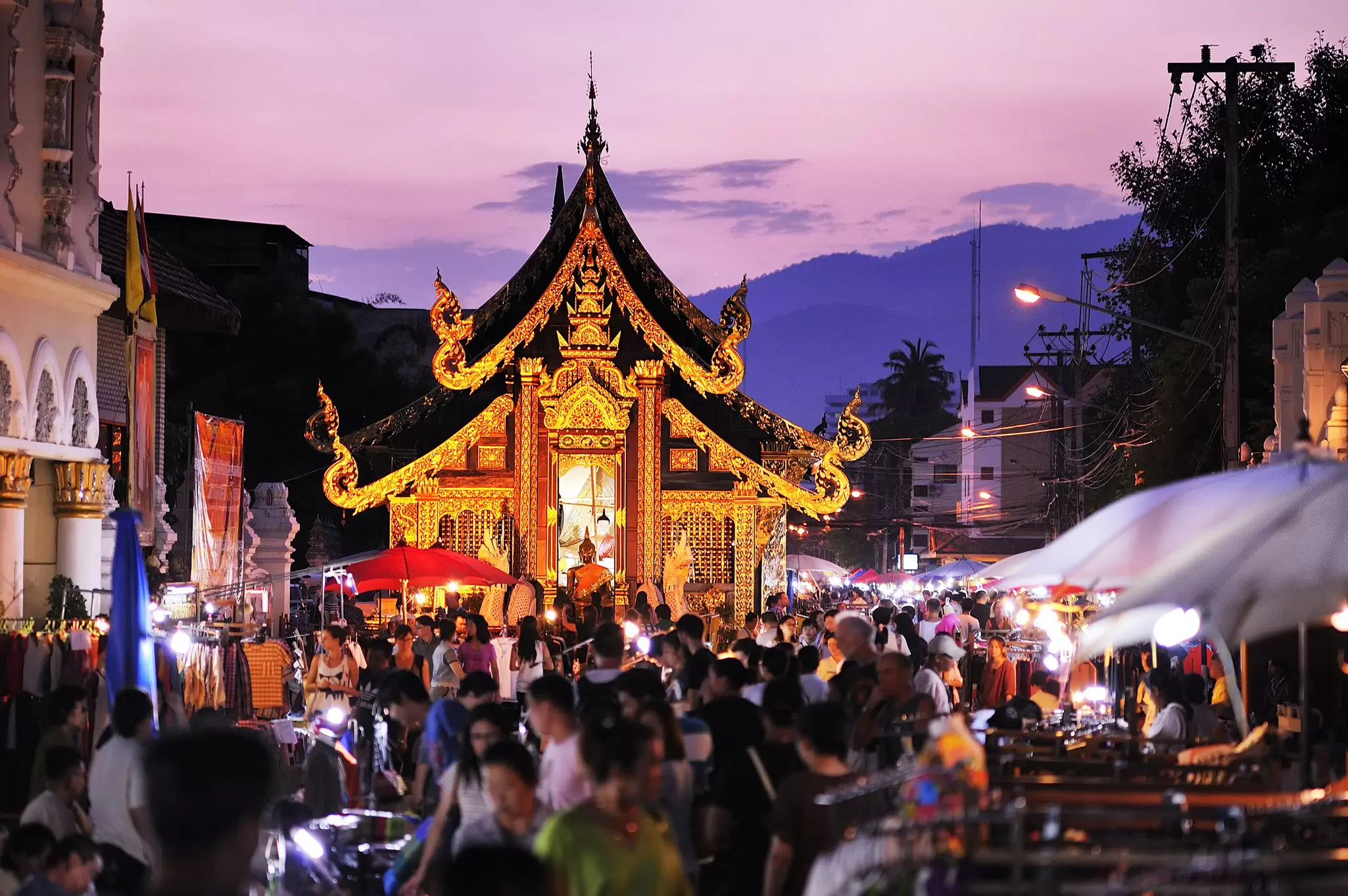 A golden prayer hall surrounded by market stalls in Chiang Mai, Thailand.
