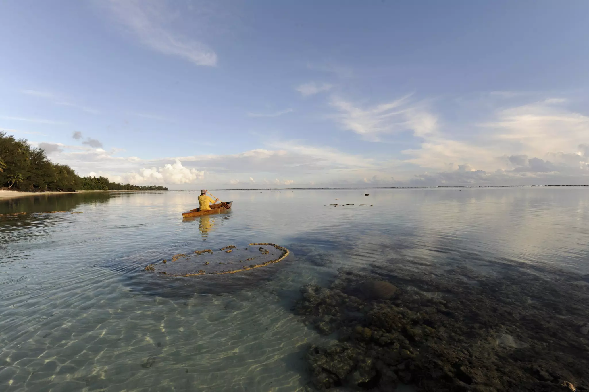 Man paddling canoe on Raratonga coast.