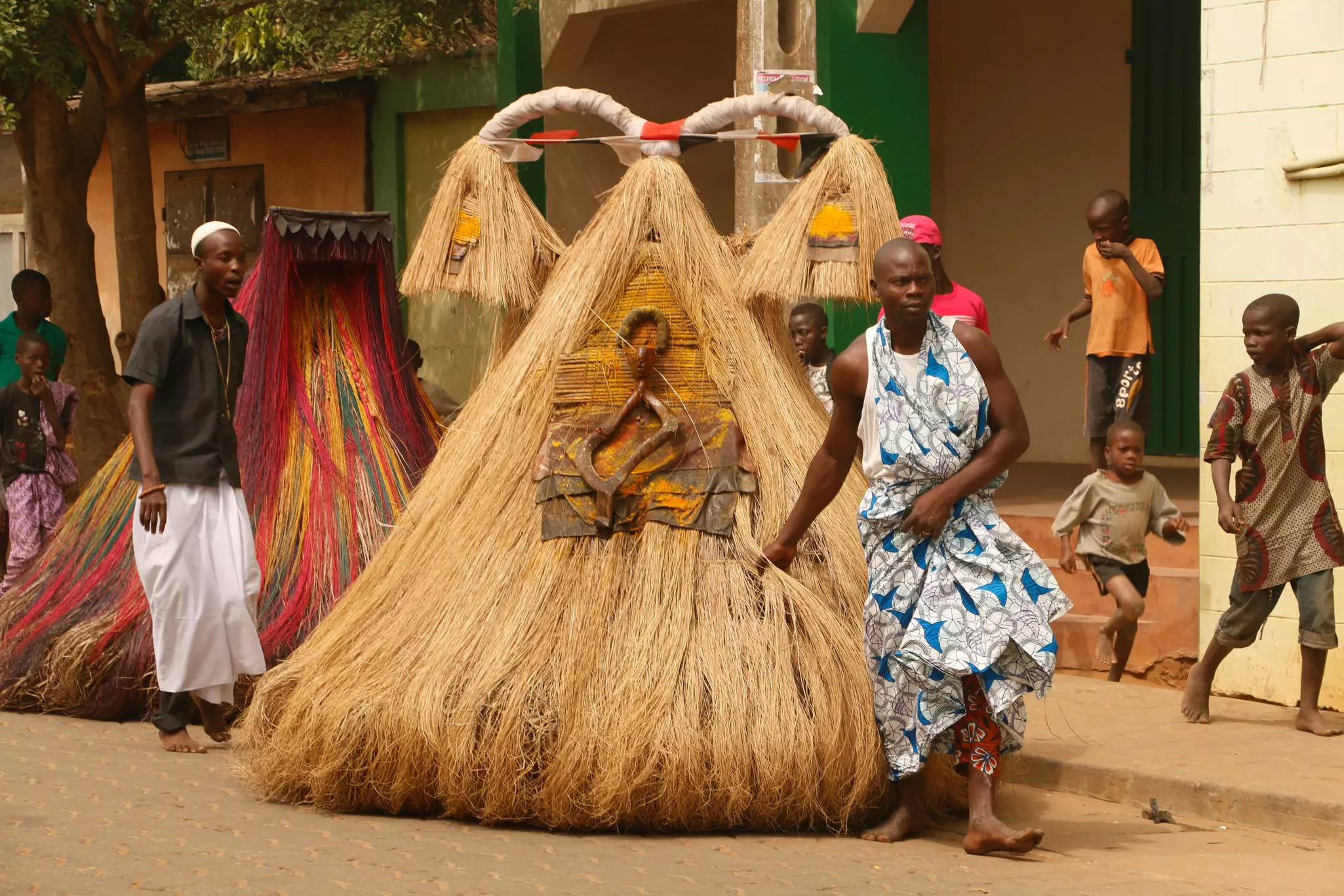 People walk on a city street leading straw-covered creations that represent spirits.