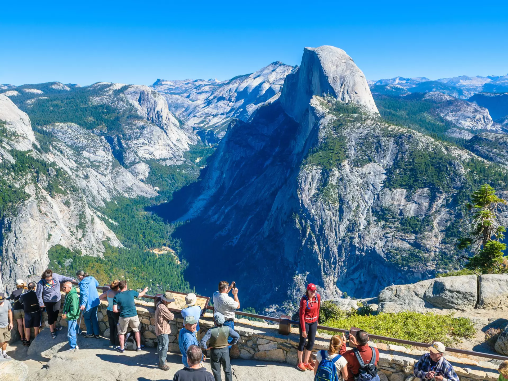 Visitors gather at Glacier Point with the Half Dome mountain in the background.