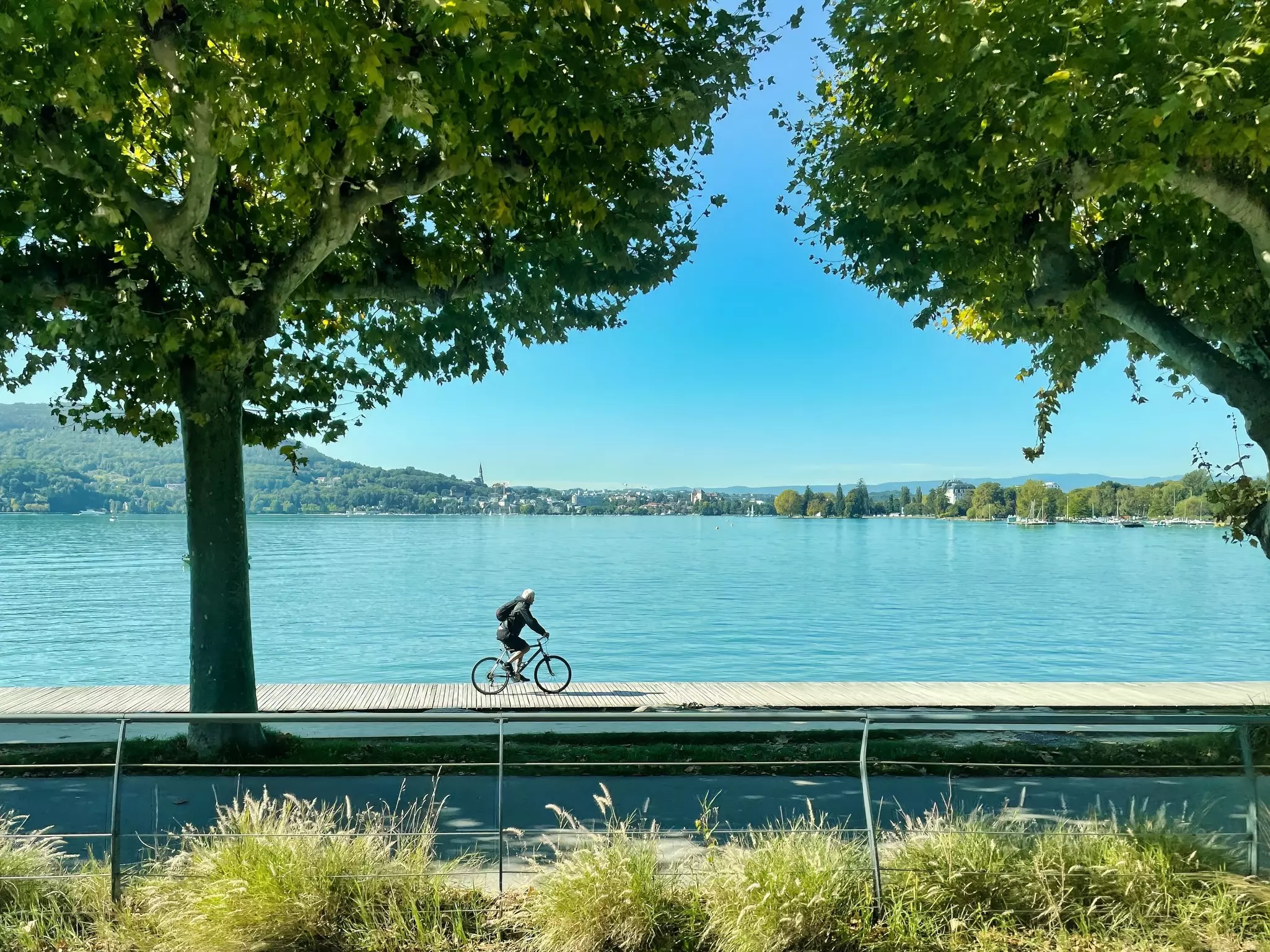 a cyclist is riding on his bicycle on a board walk a long the lake of annecy 