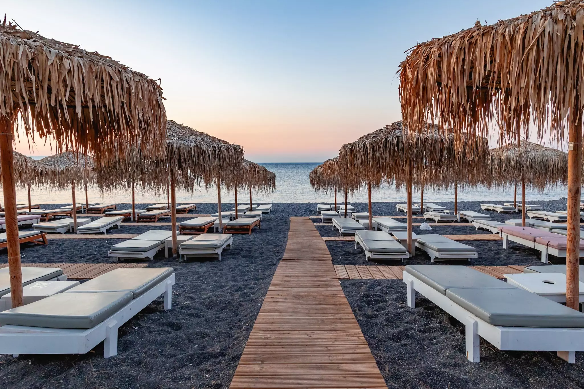 Black sand beach with rows of cushioned loungers under straw umbrellas