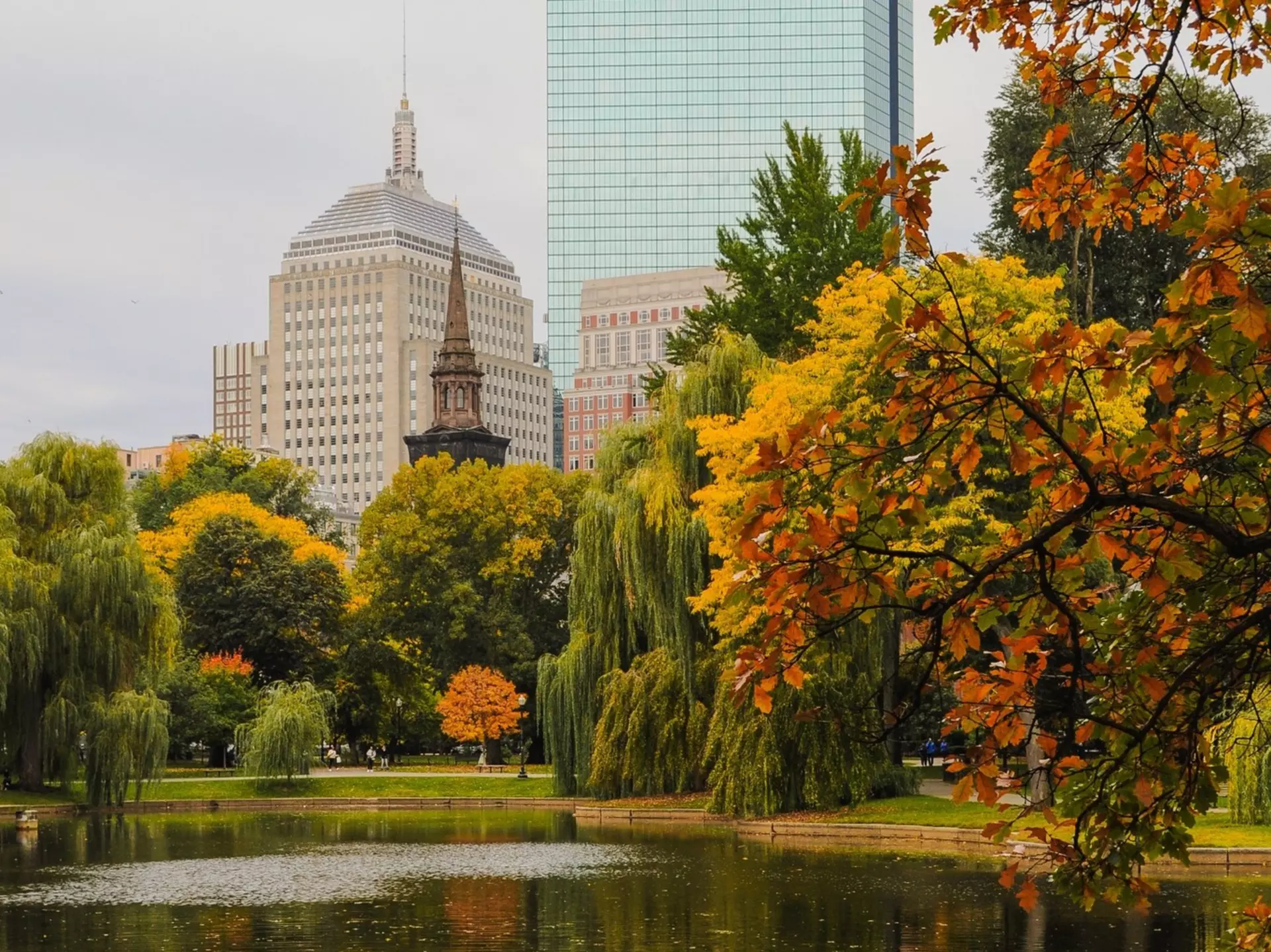 A lake in a park is surrounded by trees with autumn leaves.