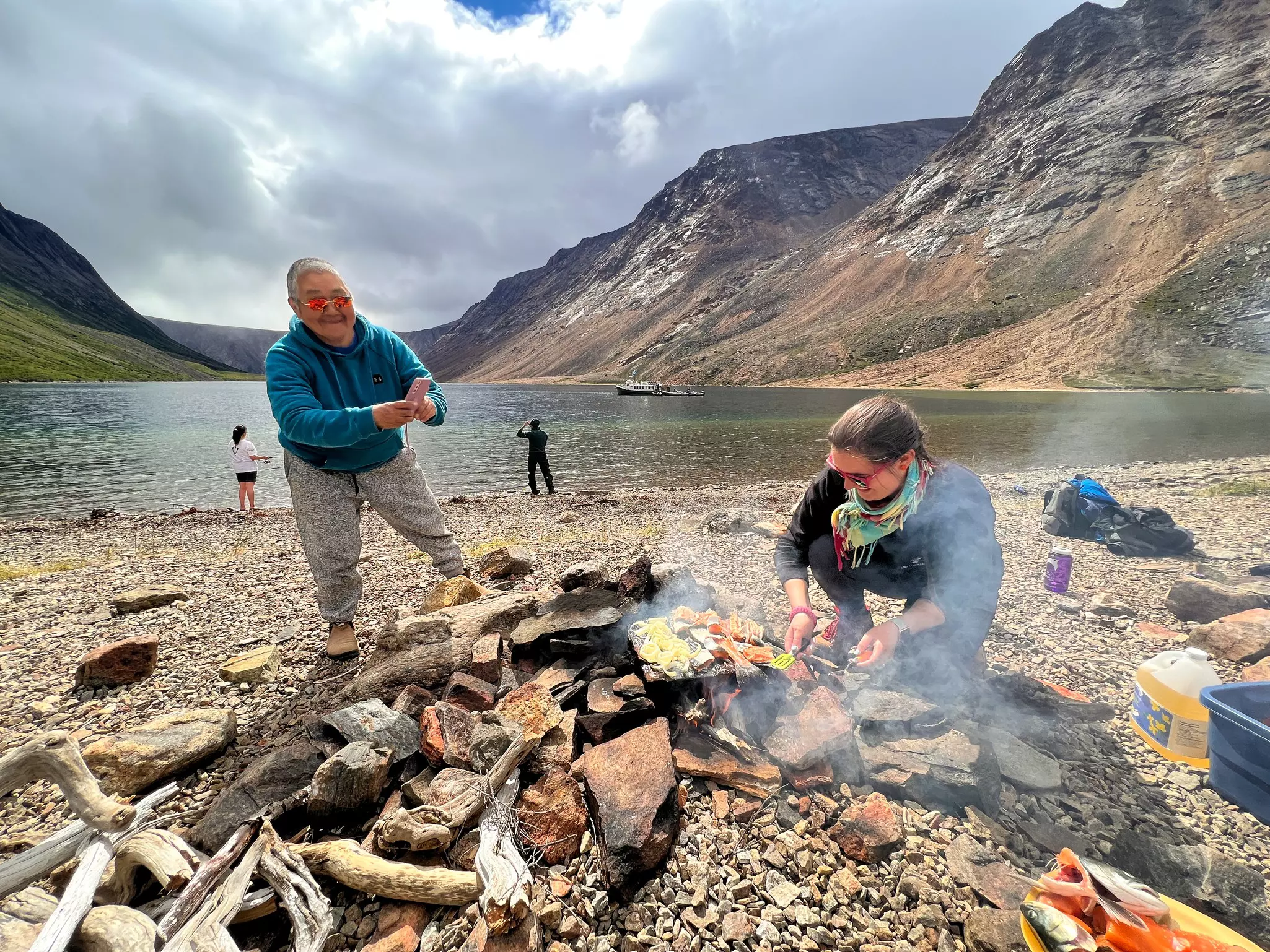 Cultural Ambassador and Bear Guard Maria shapes panitsiak bread for frying, alongside a Park Canada staffer cooking freshly-caught char © Liz Beatty