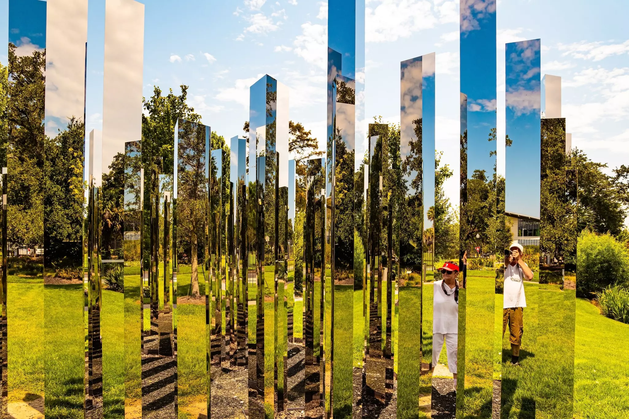The images of viewers are reflected in mirrored columns, part of an outdoor art sculpture in a park in New Orleans