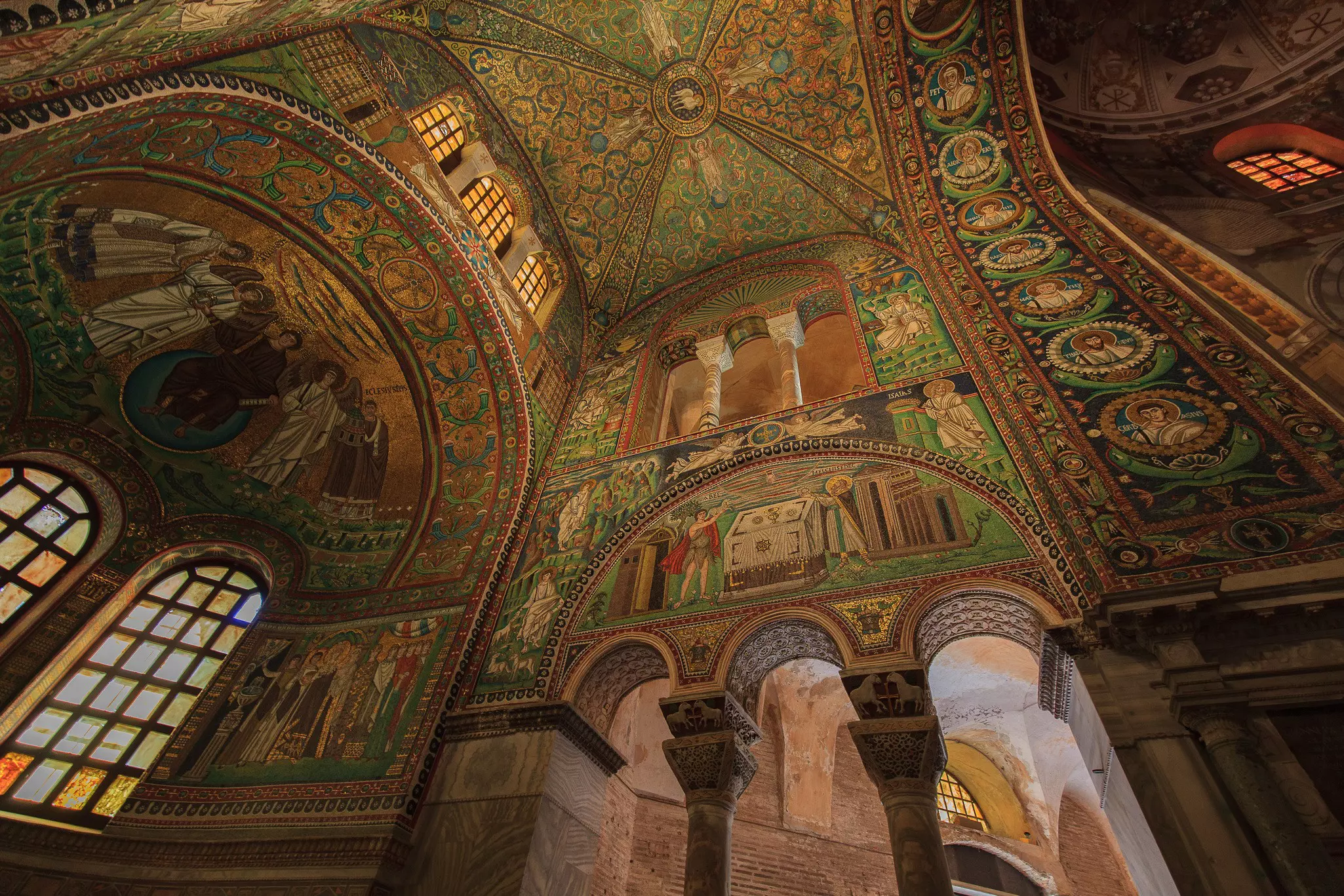 The ceiling and walls of an ancient church covered in beautiful mosaics in shades of green and gold