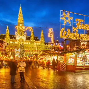 An illuminated Christmas market with a sign of lights spelling out Frohe Weihnachten, which means Merry Christmas in German