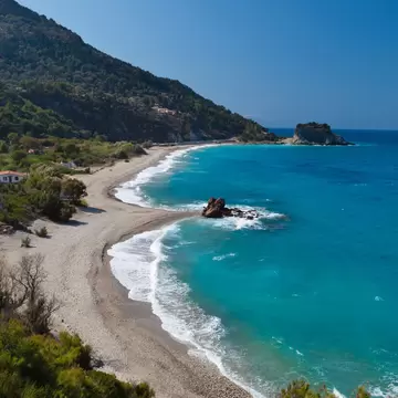 Curved pebble beach with turquoise surf, a rocky islet and wooded hillside at Potami near Karlovasi, Samos.