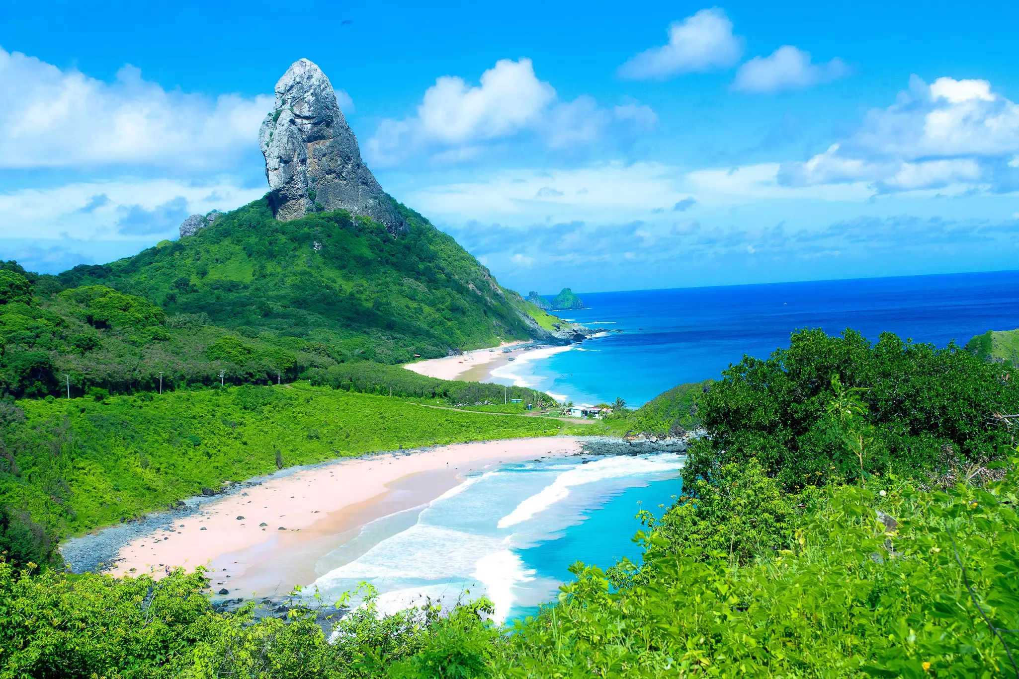 A large rocky outcrop covered in greenery stands tall above two golden-sand beaches
