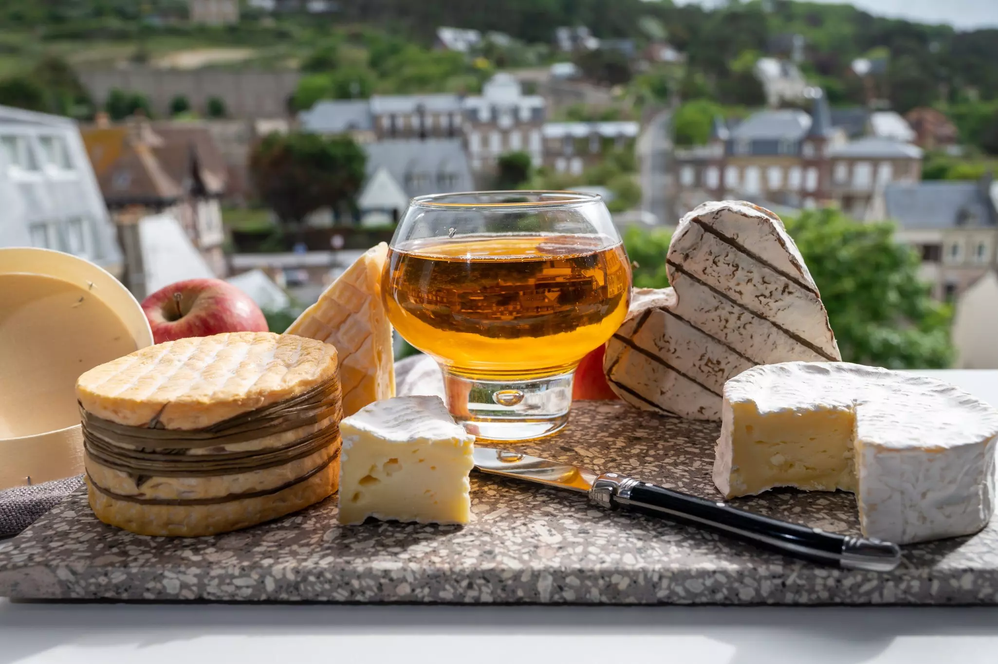 Cheeses and a glass of apple cider, with houses of Étretat in the background