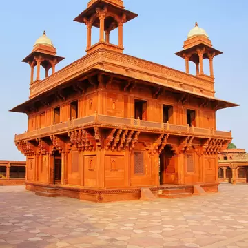 A two-storey red sandstone pavilion with four domed rooftop kiosks on a chequered stone courtyard at Fatehpur Sikri, India.