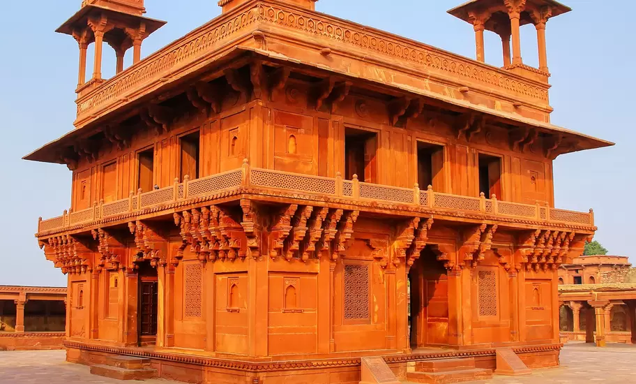 A two-storey red sandstone pavilion with four domed rooftop kiosks on a chequered stone courtyard at Fatehpur Sikri, India.