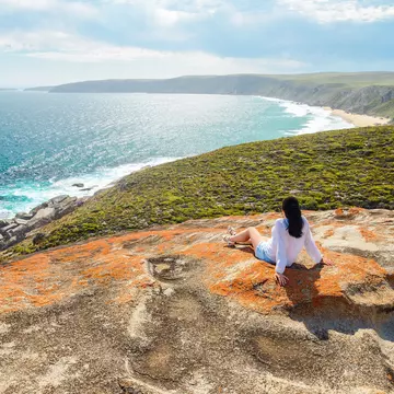 A woman sits on a clifftop looking out at the coastal scenery